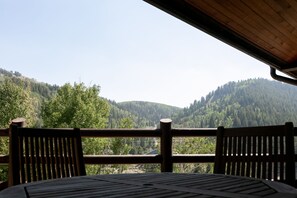 Eine Holzterrasse mit Tisch und Stühlen mit Blick auf einen bewaldeten Berg.