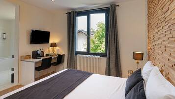 A hotel room with a bed, a desk with a chair, a television, and a window with curtains.