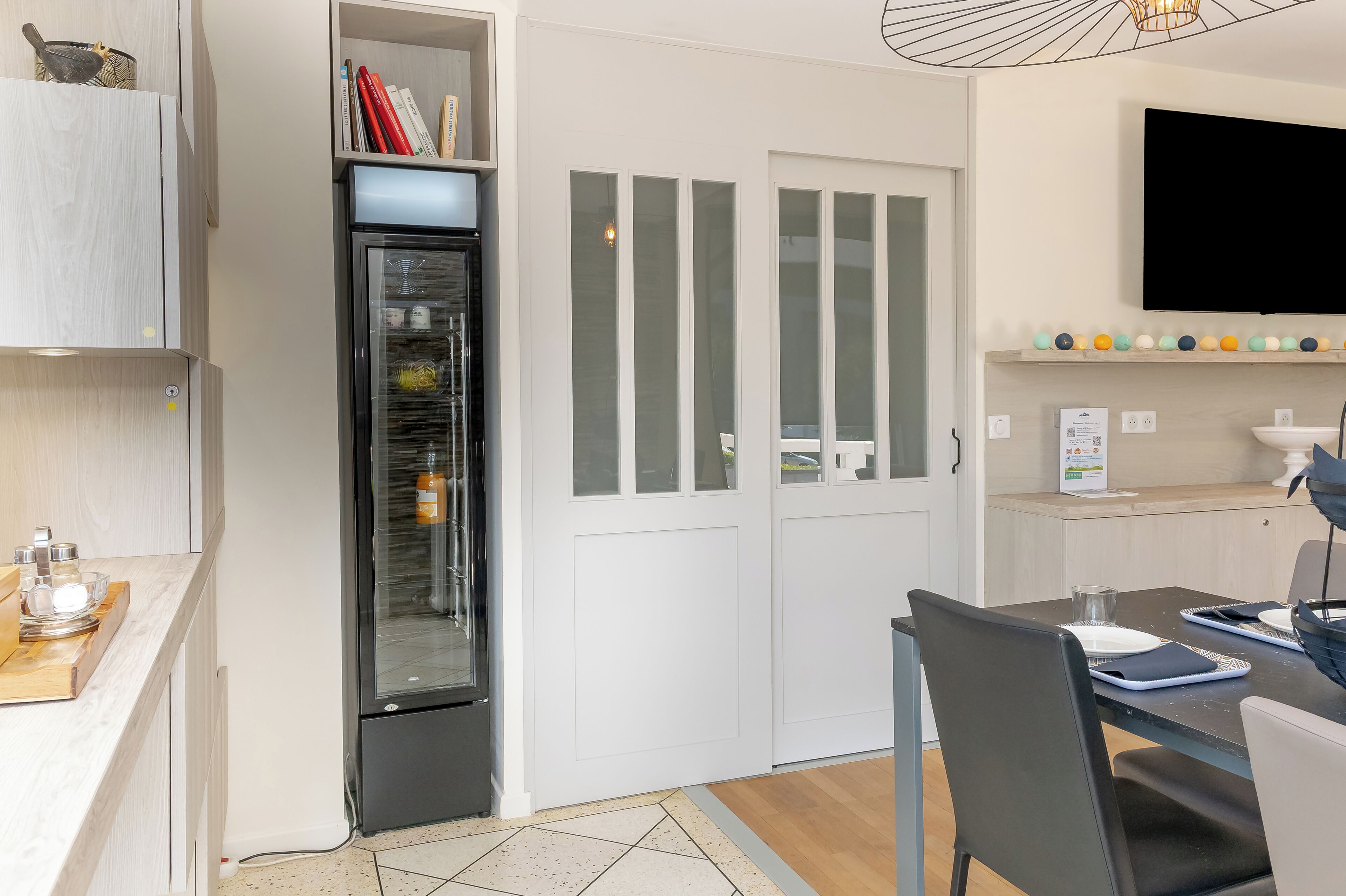 A compact kitchen with a built-in refrigerator, a dining area with a table and chairs, and a TV mounted on the wall.