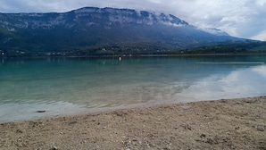 Ein See mit einem Berg im Hintergrund und einem kiesigen Ufer im Vordergrund.
