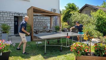 Mesa de ping pong montada en un jardín con un muro de piedra y una pérgola de madera.