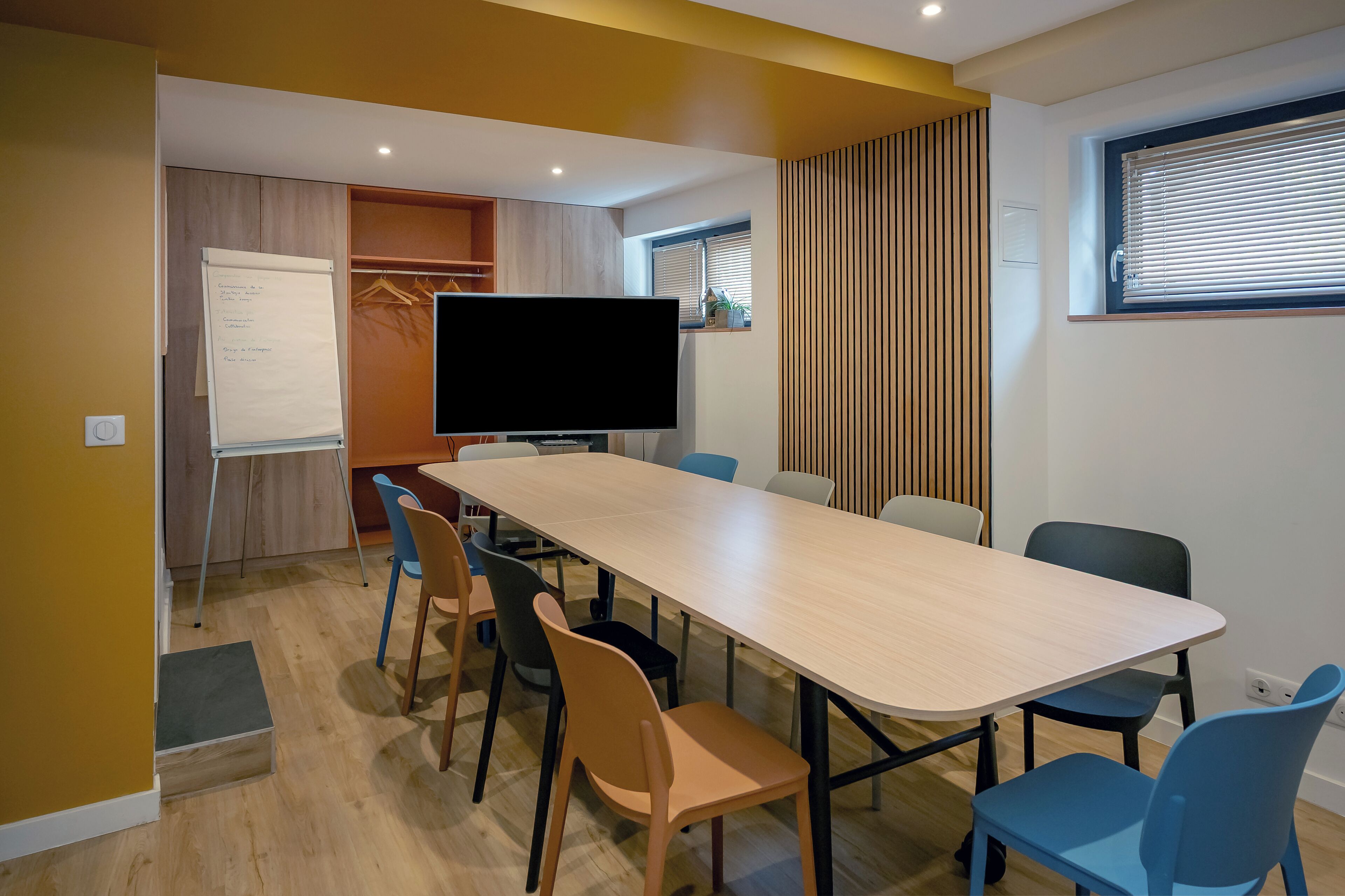 A conference room with a long table, chairs, a whiteboard, and a television.