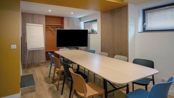 A conference room with a long table, chairs, a whiteboard, and a television.