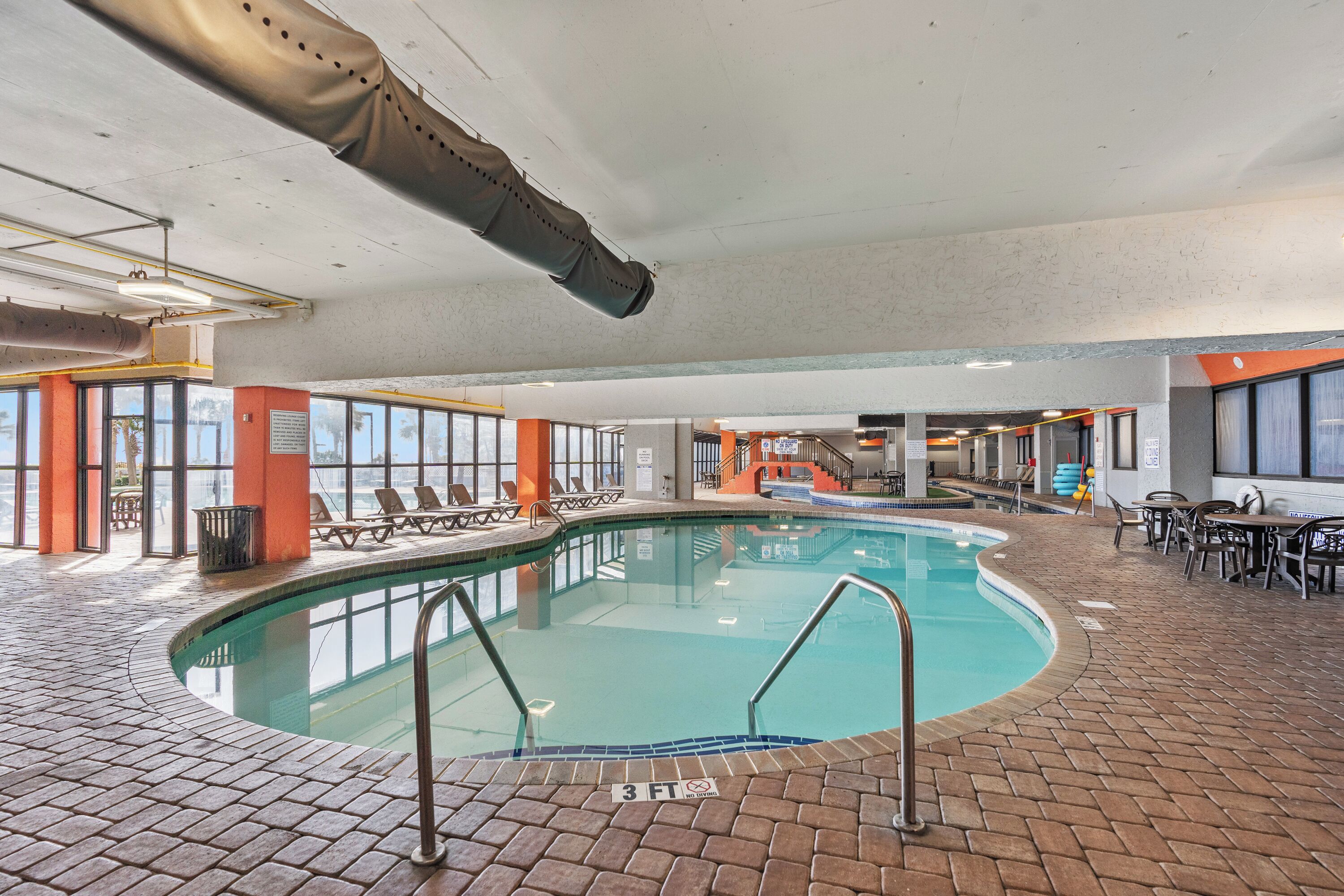 An indoor swimming pool with a brick floor, clear water, and a 3 ft depth marker.