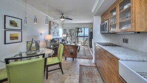 Uma cozinha moderna com armários de madeira, bancada de mármore e um espaço de refeições com mesa e cadeiras de vidro.