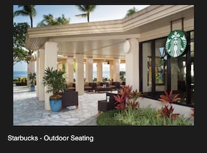 An outdoor seating area with tables and chairs, potted plants, and a Starbucks logo.