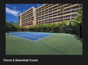 A tennis and basketball court with a multi-story building in the background.