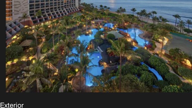 Un resort con una piscina grande rodeada de palmeras y vista al océano.