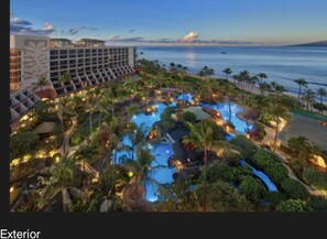 A resort with a large pool surrounded by palm trees and a view of the ocean.