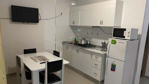 Cuina compacta amb armaris blancs, microones, nevera i taula de dinar amb cadires.
