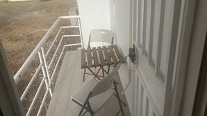 Un balcó amb una cadira blanca i una taula petita, amb vista a un edifici de parets grogues i blanques.