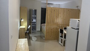 Una habitació petita i ben il·luminada amb escriptori de fusta, cadira, llit i microones.