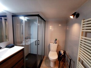 Ein Badezimmer mit Duschkabine aus Glas, Toilette und Waschbecken mit Spiegel.