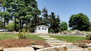 A small white building with a stone pathway leading to it, surrounded by trees and a grassy area. - Gite Chez Marius (Saint-Agrève)