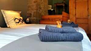 A neatly made bed with folded towels, a stone wall, and wooden furniture in a room. - Gite Chez Marius (Saint-Agrève)