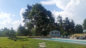 A swimming pool with a stone pathway leading to it, surrounded by a grassy lawn and trees. - Gite Chez Marius (Saint-Agrève)