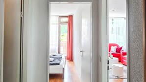 Ein Flur mit einem Bett, einem roten Sofa und einem weißen Sessel im angrenzenden Zimmer.