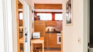 Ein schmaler Flur führt zu einer Küche mit Holzschränken, einem Tisch und einer Mikrowelle.