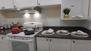 Une cuisine avec des meubles blancs, un fourneau et un plan de travail sur lequel se trouvent trois assiettes de nourriture.