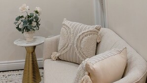 Un salon avec un canapé beige, une table ronde ornée d’un vase de fleurs et un tableau accroché au mur.