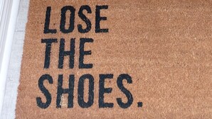 Un escalier avec un paillasson sur lequel on peut lire : « ENLEVEZ VOS CHAUSSURES ».