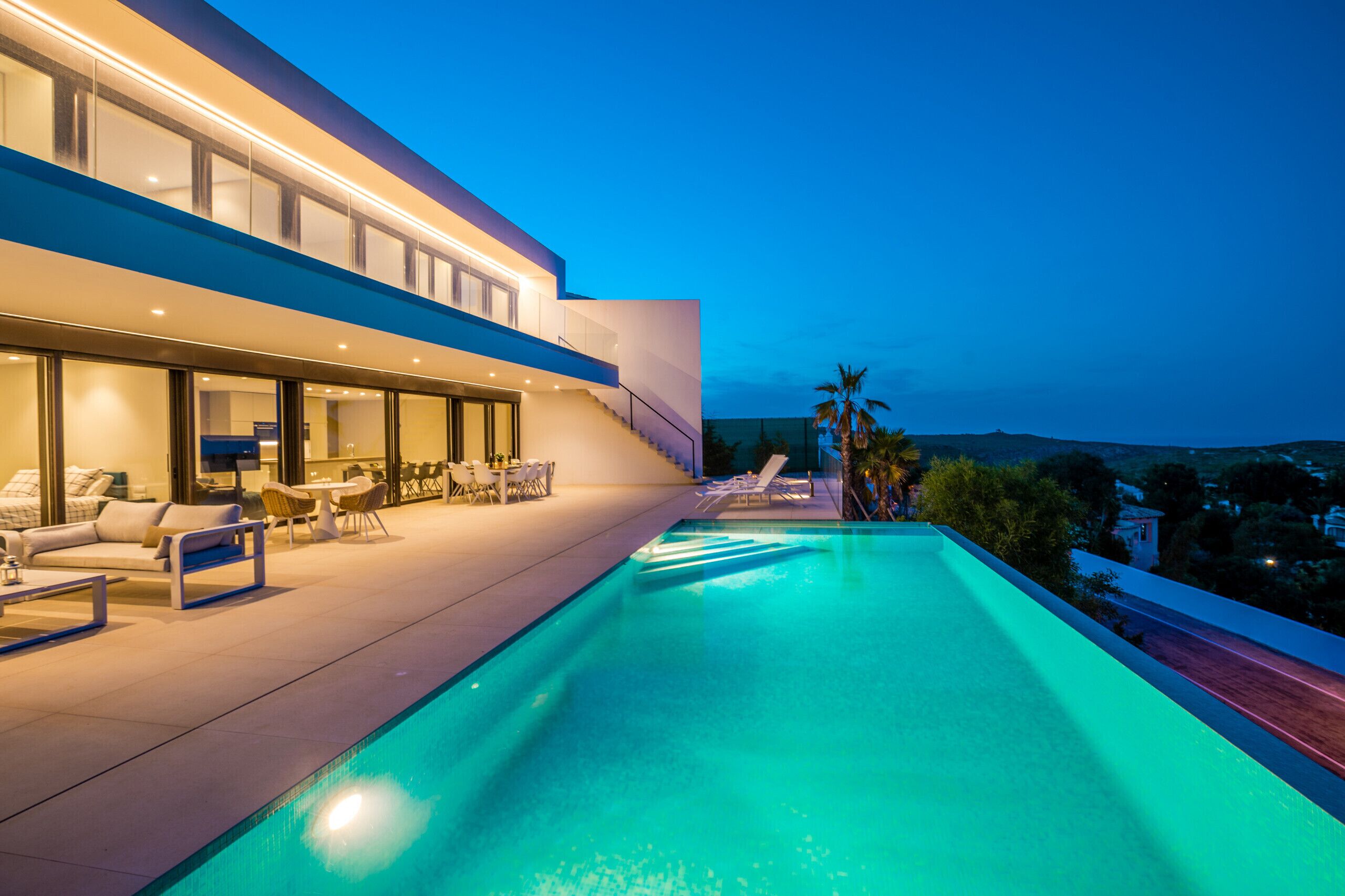 A modern house with a swimming pool, outdoor seating, and a view of the landscape.