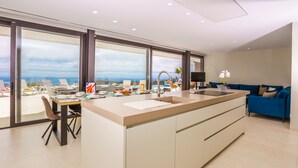 A modern kitchen with a large island, a dining area with chairs, and a view of the ocean through large windows.