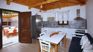 A kitchen with wooden beams, a dining table, chairs, a refrigerator, and a stove. - Perfect for peace and quiet,in the countryside (ΣΚΟΠΕΛΟΣ)