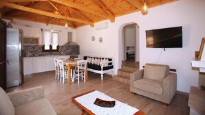 A spacious living area with a wooden ceiling, a dining table, a sofa, and a TV mounted on the wall. - Perfect for peace and quiet,in the countryside (ΣΚΟΠΕΛΟΣ)