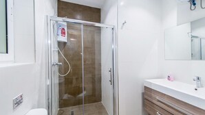 Ein modernes Badezimmer mit einer Duschkabine, einem weißen Waschbecken mit Spiegel und einer Holzkommode.