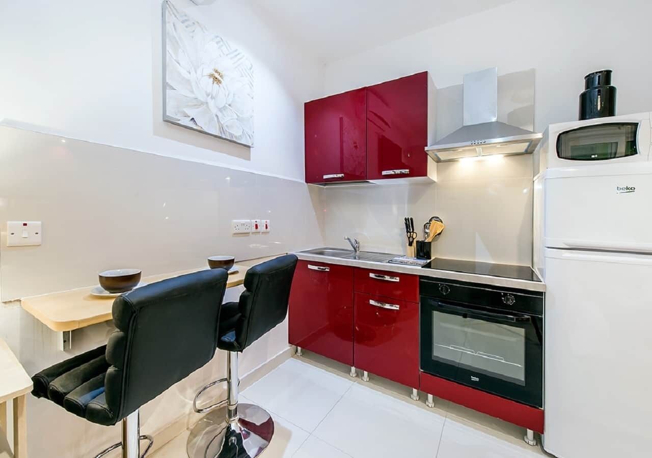 A compact kitchen with red cabinets, a black oven, and a white refrigerator.