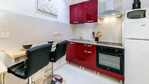 Eine kompakte Küche mit roten Schränken, einem schwarzen Backofen und einem weißen Kühlschrank.