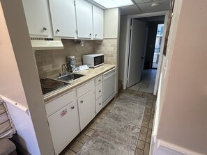 Una cocina con armarios blancos, microondas y pileta.