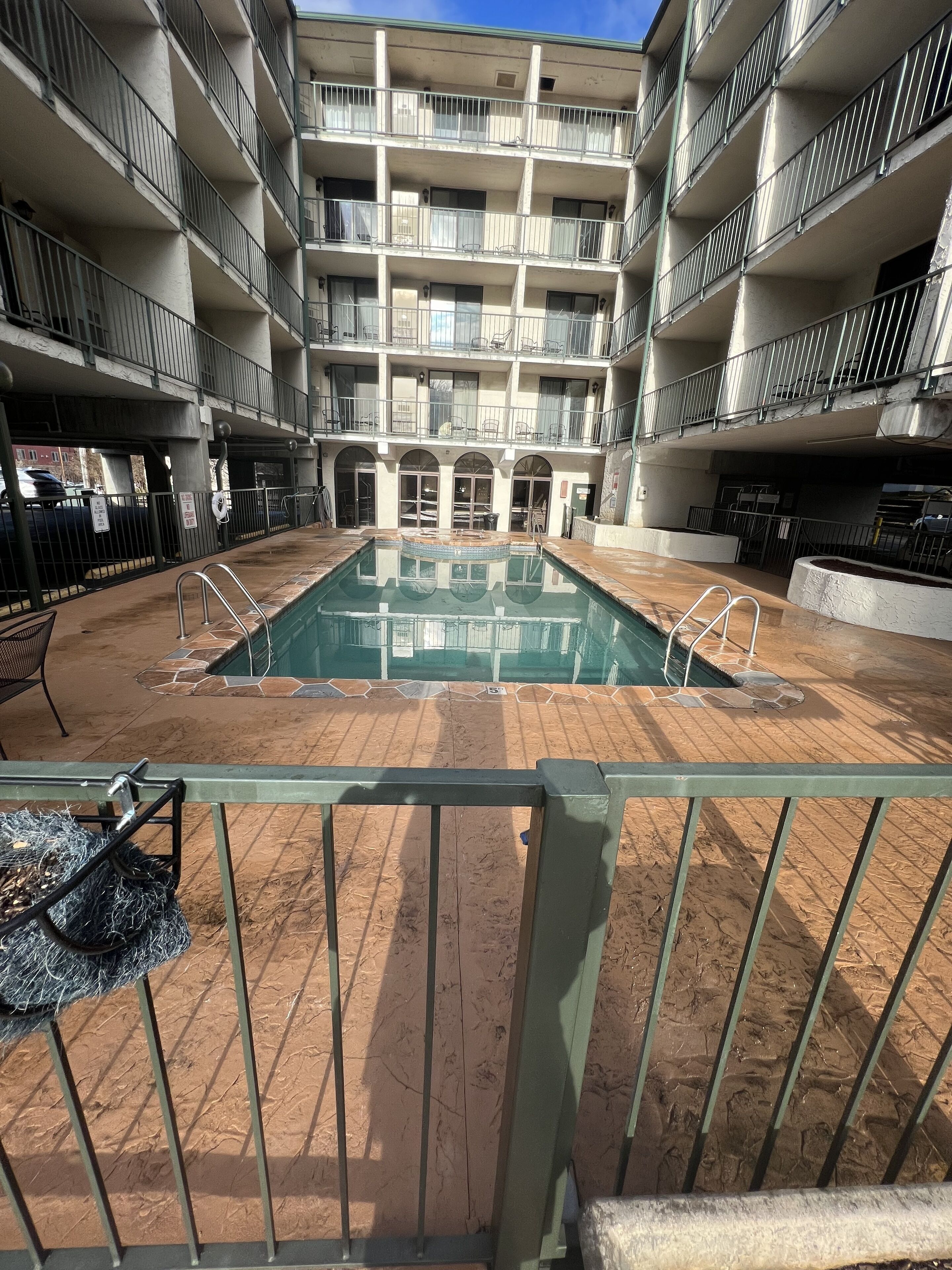 A multi-story building with a central courtyard featuring a swimming pool, surrounded by balconies and outdoor seating.