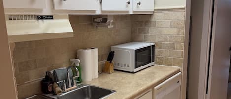 Una cocina con armarios blancos, microondas, fregadero y lavavajillas.
