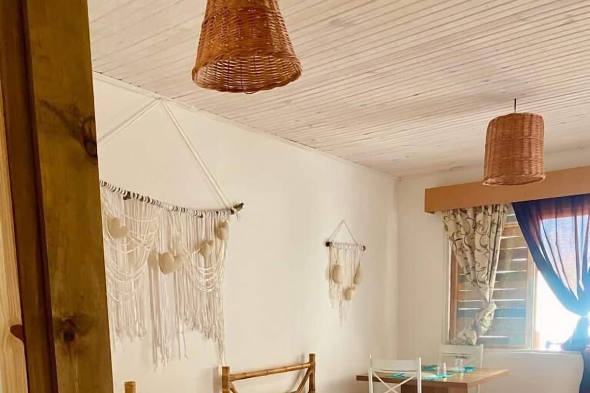 Quarto aconchegante com duas camas, uma mesa pequena e peças de macramé nas paredes.