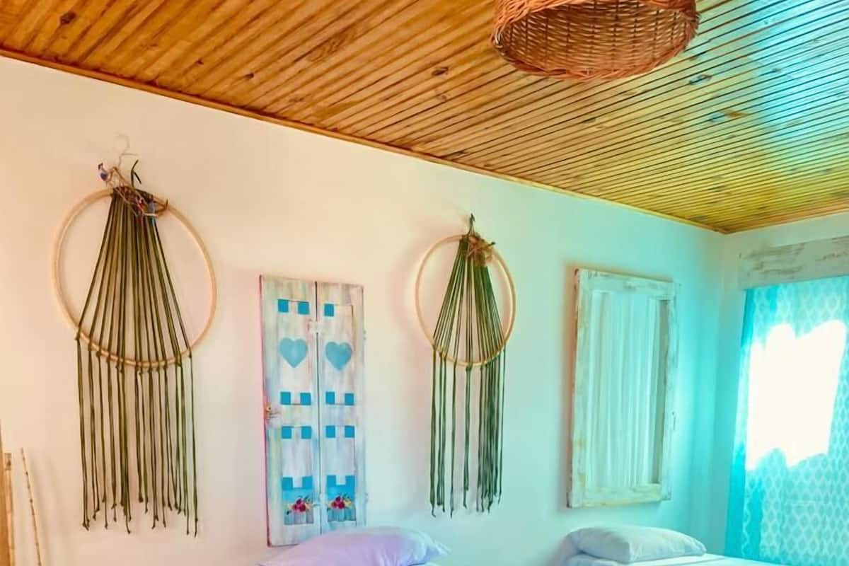 Um quarto aconchegante com duas camas, um cobertor listrado e colorido e tapeçarias de macramé na parede.