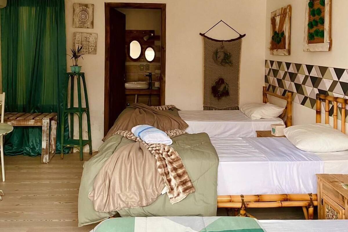 Quarto com duas camas, cômoda de madeira, cadeira verde e uma pequena mesa.