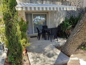 Une terrasse avec une table et des chaises, entourée de plantes en pot et d’un arbre.