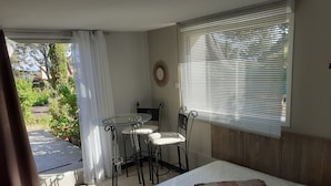 Ein Schlafzimmer mit einem Bett, einem Glastisch mit Stühlen, einem Fenster mit Jalousien und Blick ins Freie.