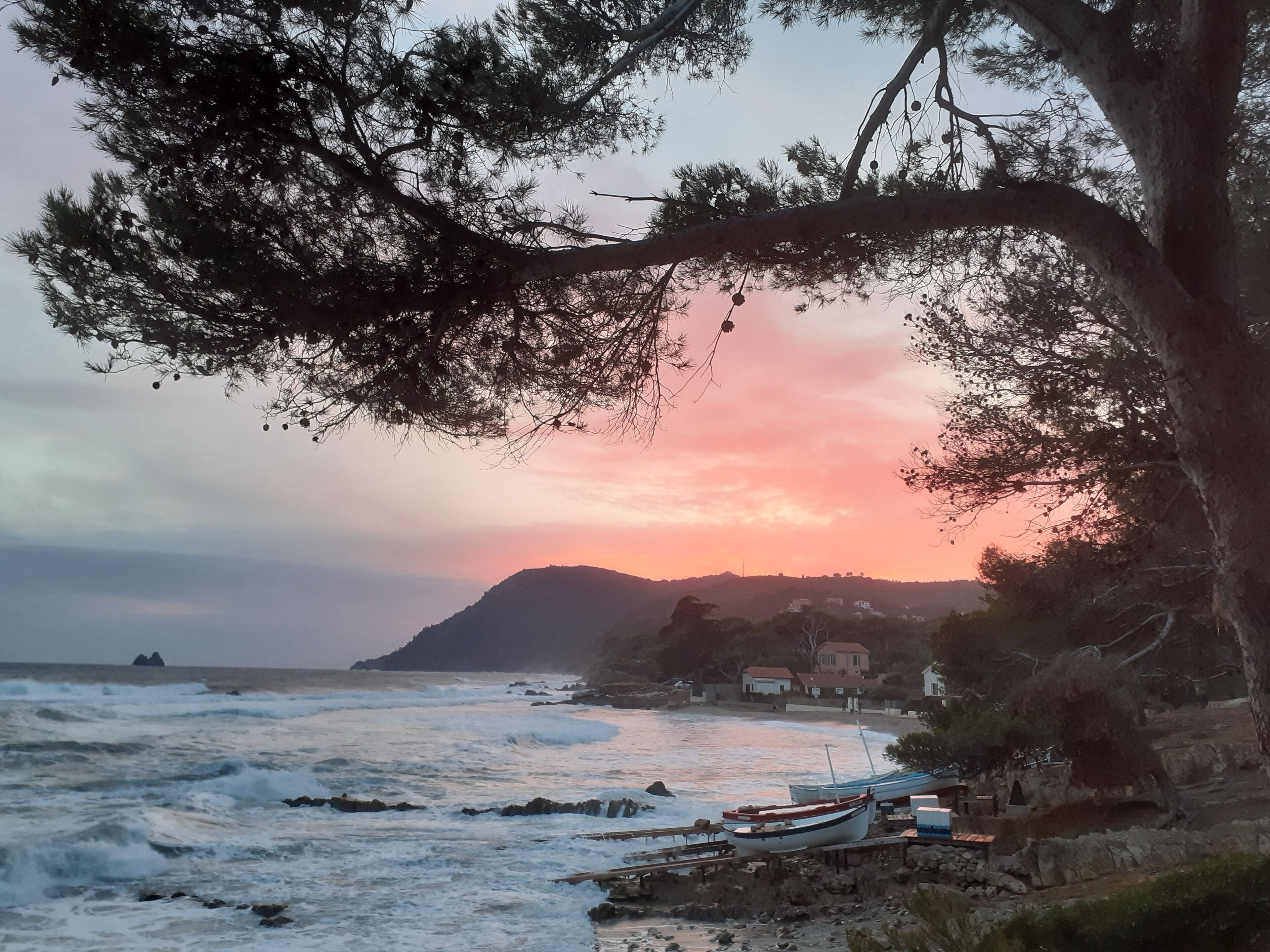 A coastal scene with a sunset, rocky shoreline, and boats.