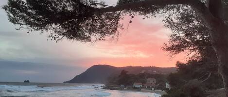 A coastal scene with a sunset, rocky shoreline, and boats.