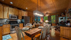 Interior de una cabaña de madera con cocina, comedor y grandes ventanales.