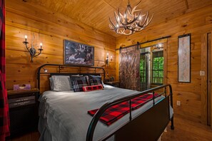 A wooden cabin bedroom with a bed, a chandelier, a map, and a painting on the wall.