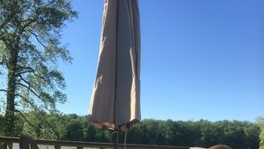 Een houten terras met een glazen tafel en stoelen, een parasol en uitzicht op een meer.