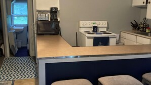 Een compacte keuken met een centraal kookeiland, een kookplaat en een spoelbak. Er staan twee krukken bij het eiland.