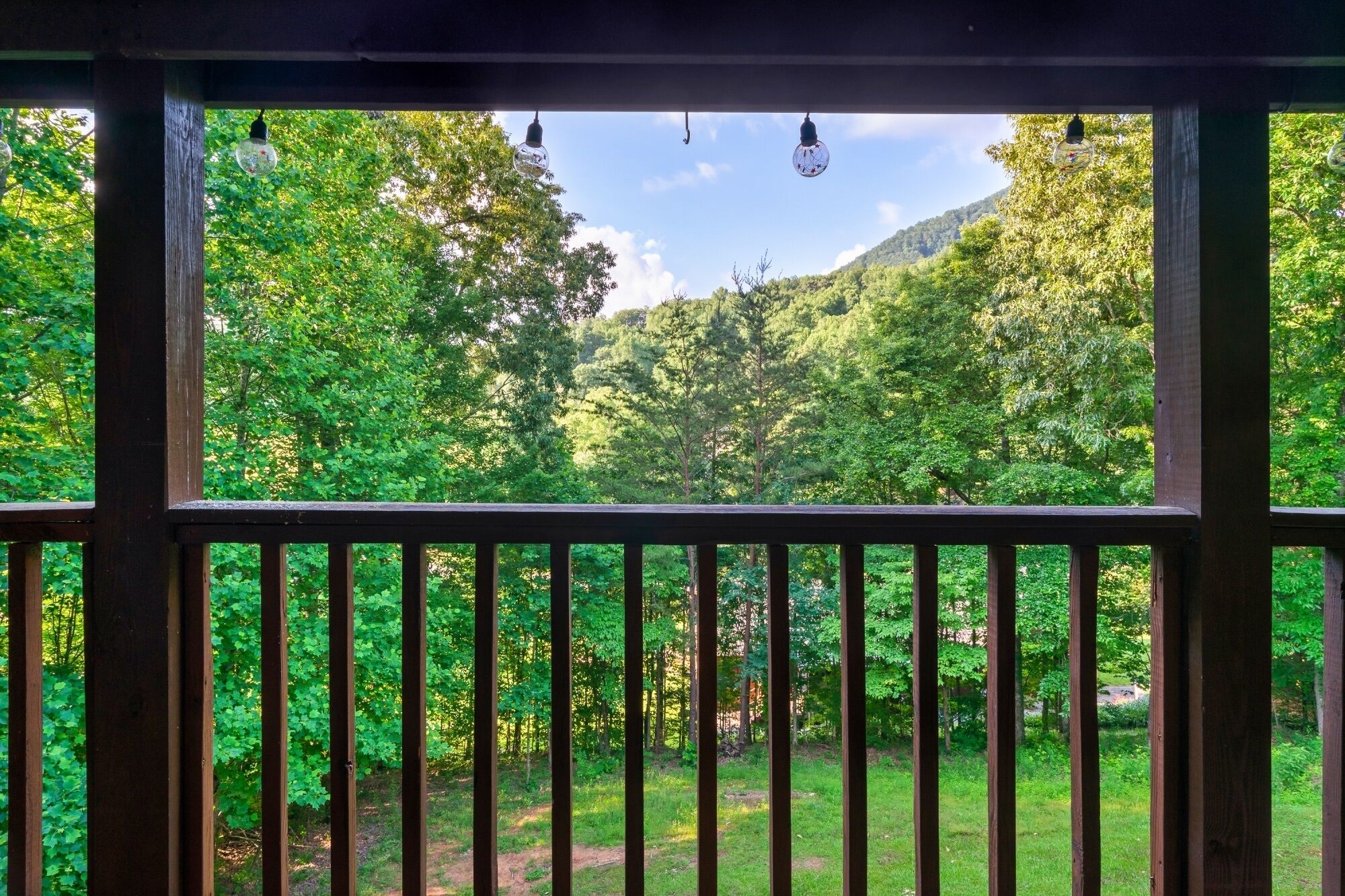 Un balcon en bois offrant une vue sur une forêt verdoyante et un ciel dégagé.