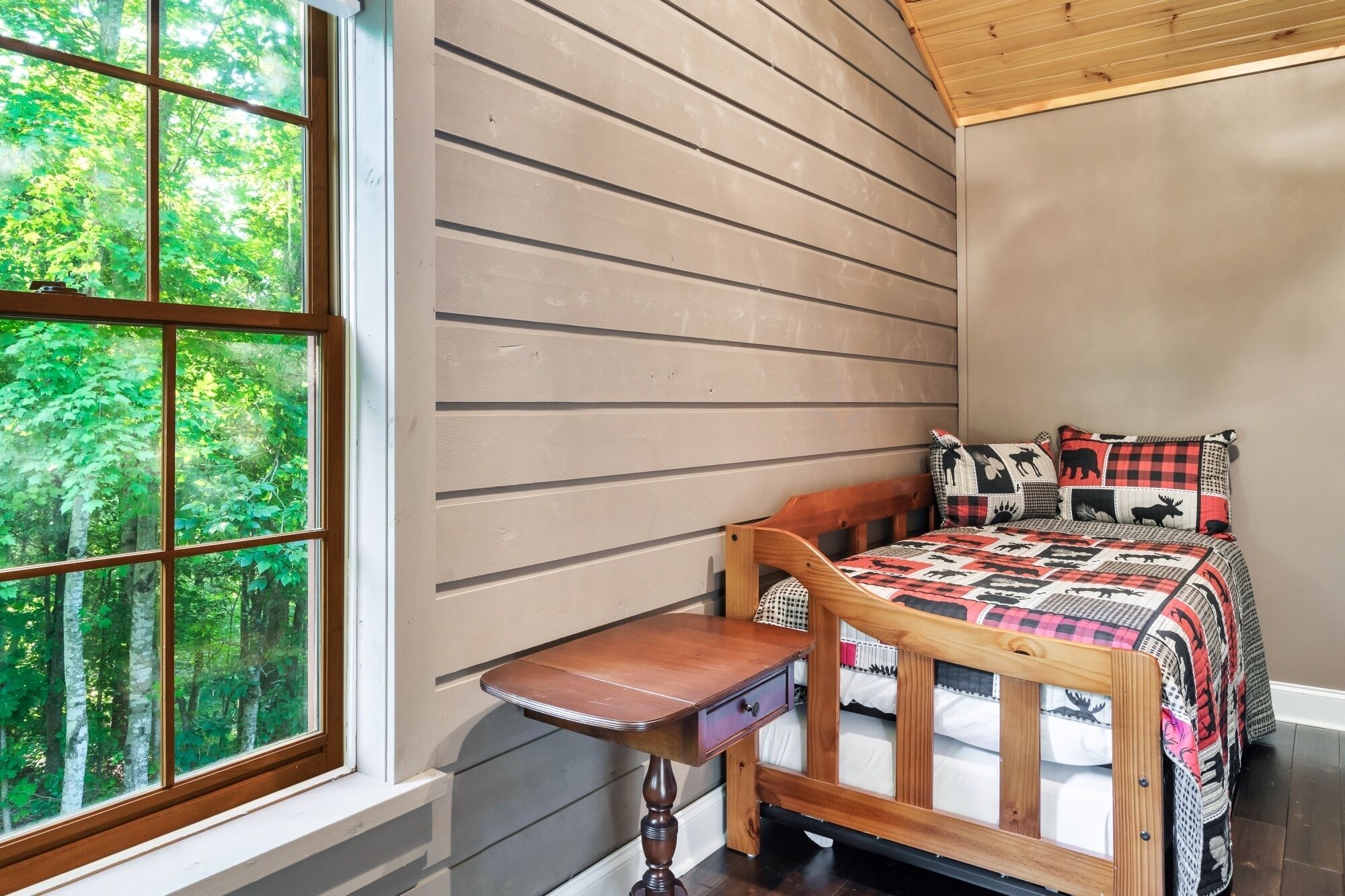 A bedroom with a wooden bed, a nightstand, and a window with a view of trees.