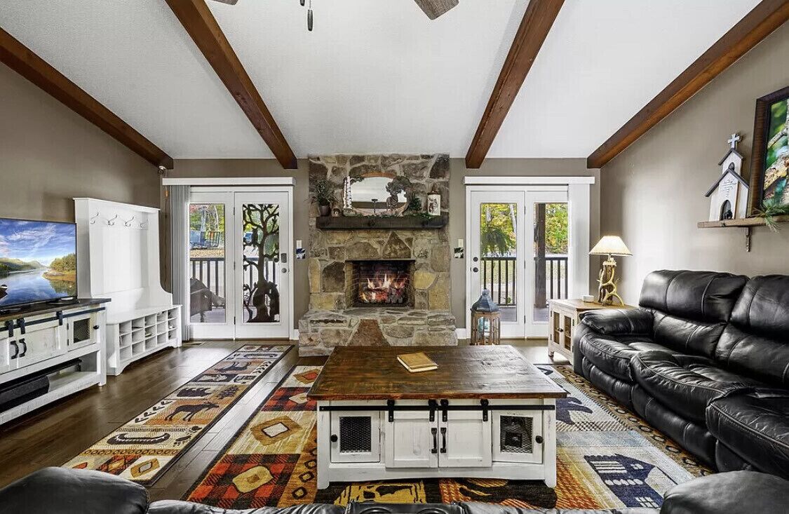 A living room with a stone fireplace, a black leather sofa, a wooden coffee table, and a patterned rug.