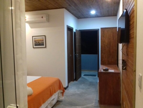A bedroom with a bed, an air conditioner, a wooden cabinet, and a television. - Pousada Barra Trip (Maraú)